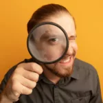 un homme nous regarde à travers une loupe, sur fond orange