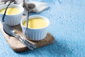 Crèmes à la vanille en ramequins blancs avec gousses de vanille, sur planche en bois